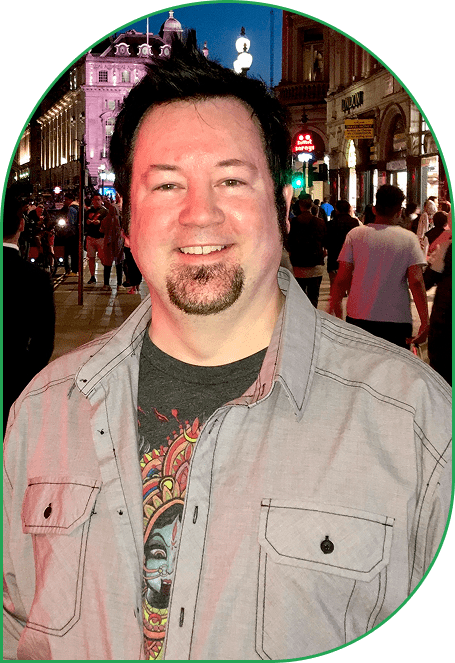 Smiling man with goatee in casual shirt at night in a lively street.